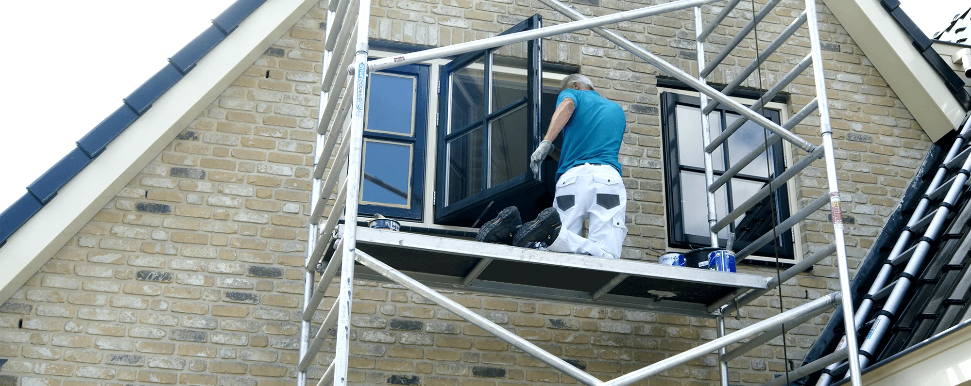 Schilder van VON Garant schildert vanaf een steiger de houten kozijnen van een woning